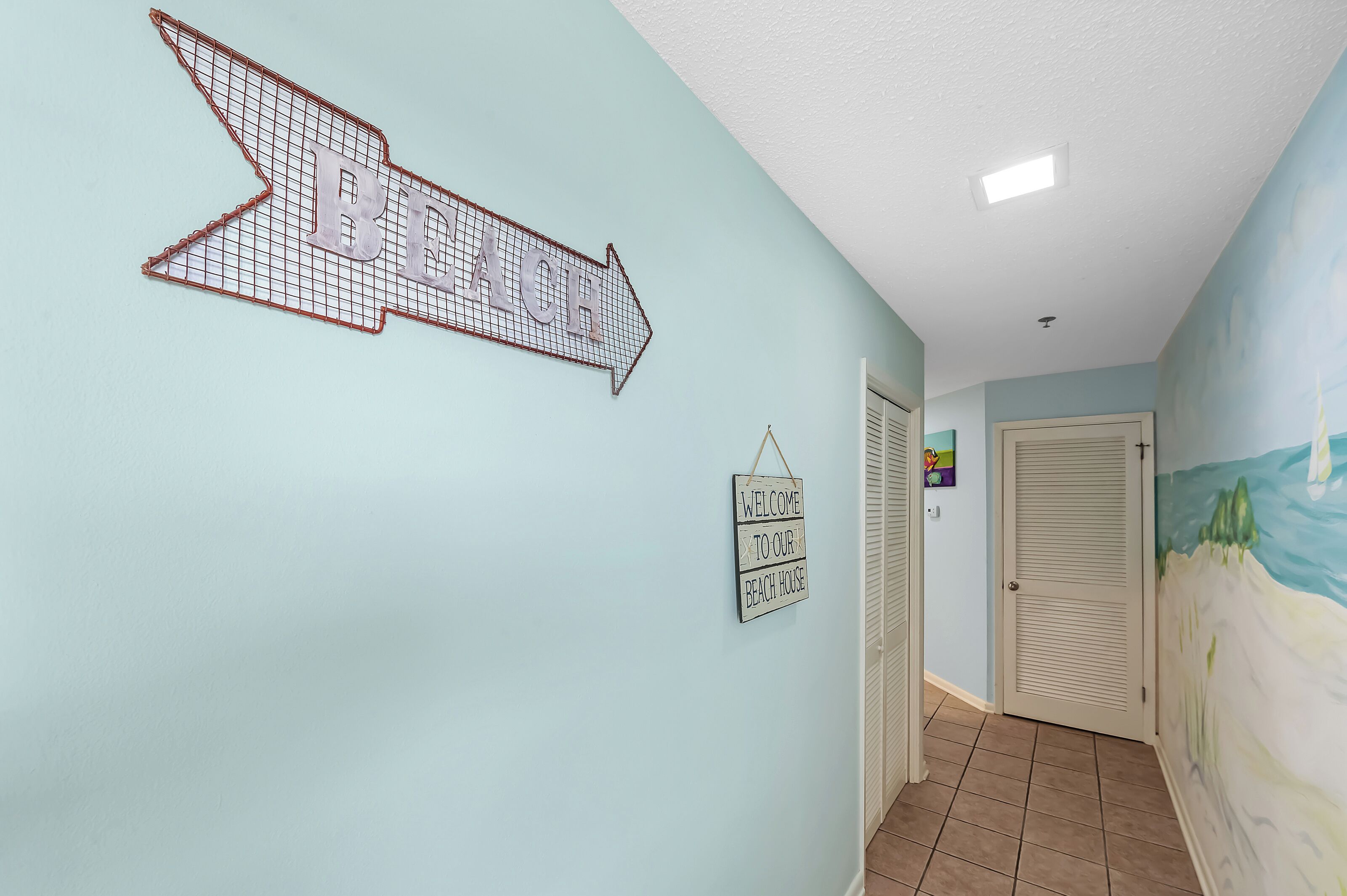 A hallway with a directional arrow sign, a welcome sign, and a beach-themed mural on the wall.