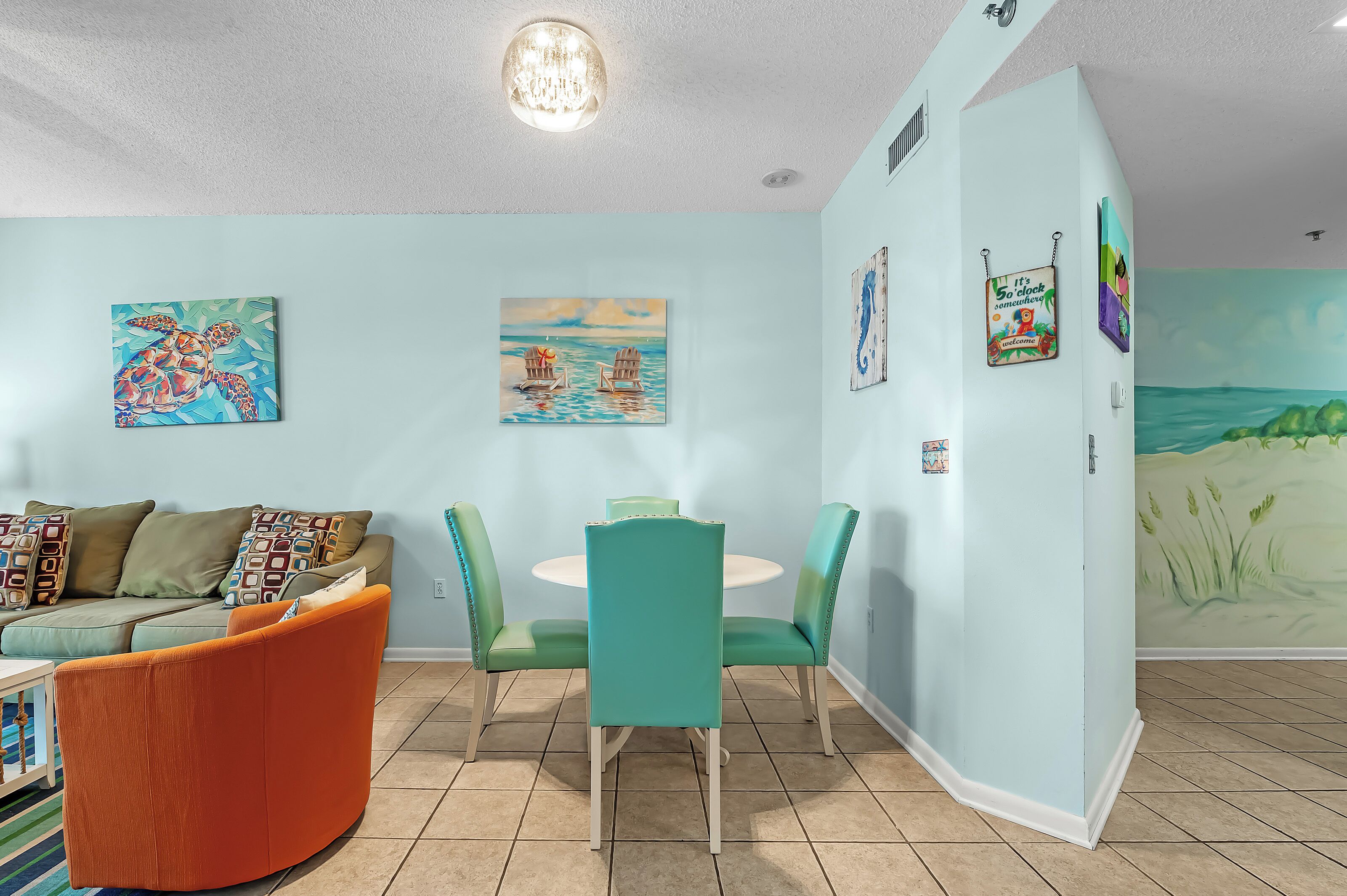 A room with teal walls, a round dining table, teal chairs, a teal sofa, and a colorful mural.