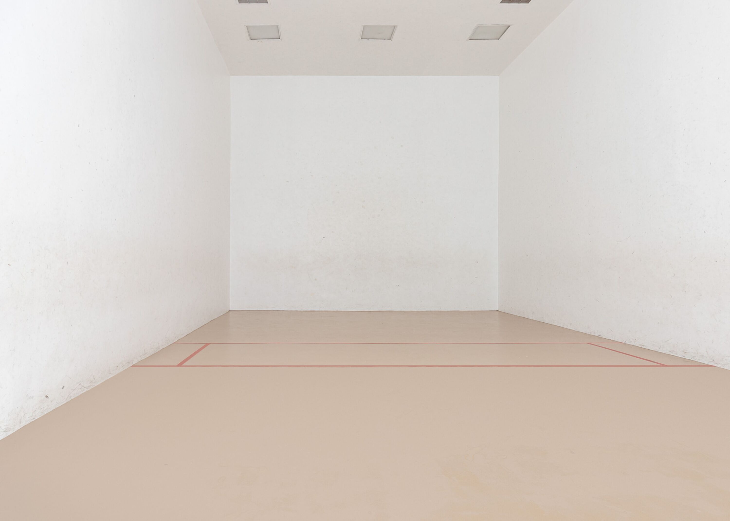 A clean, empty room with white walls and a light-colored floor, featuring a red line marking the playing area.