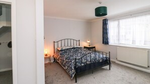 Une chambre à coucher comprenant un lit, une table de chevet, une lampe, une fenêtre avec des rideaux et un radiateur.