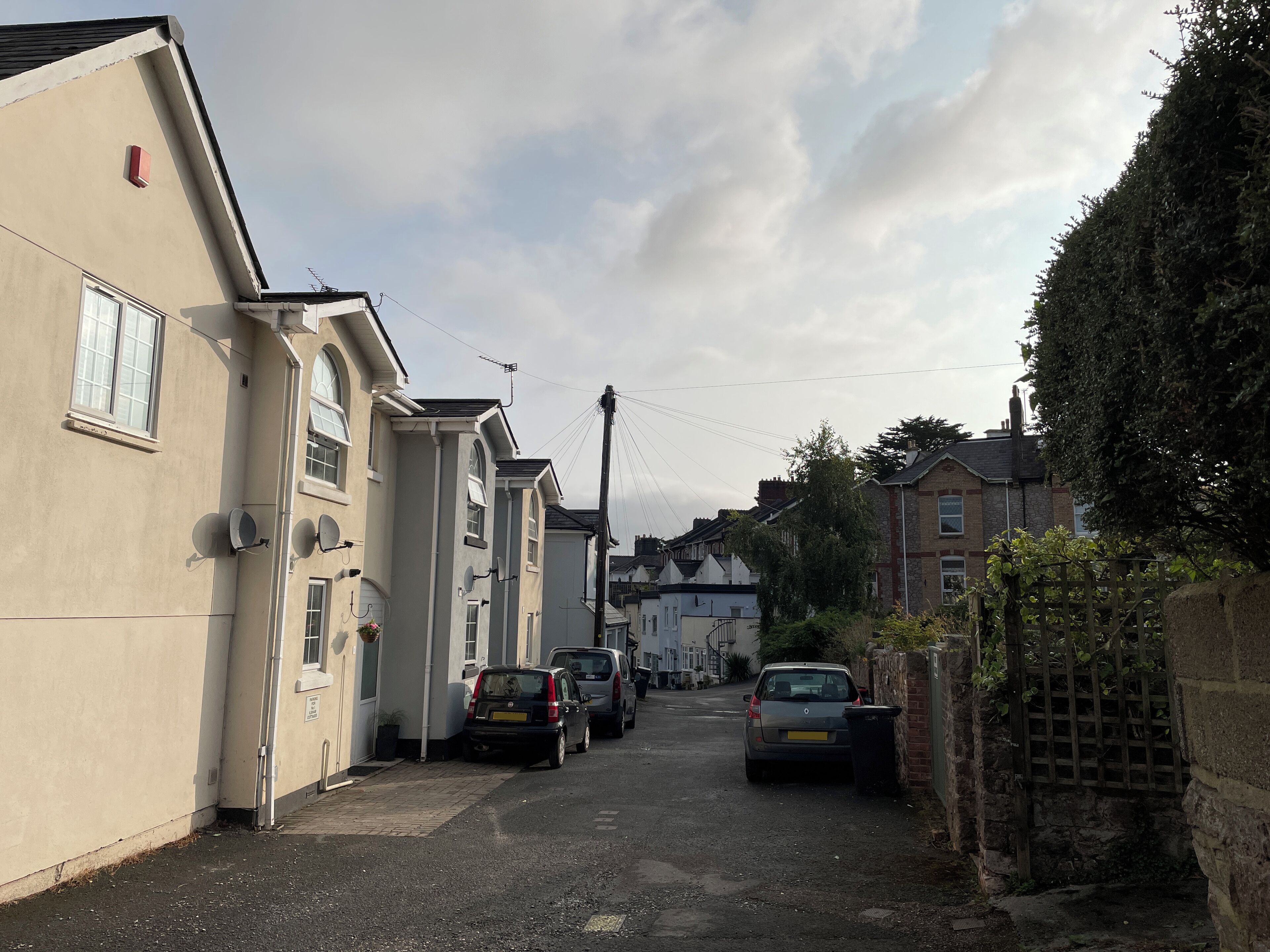 A narrow residential street with parked cars and houses on both sides.