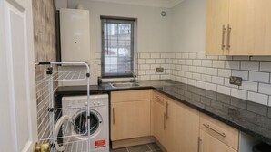 Une cuisine compacte équipée d’un lave-linge, de meubles en bois et d’une fenêtre avec des stores.