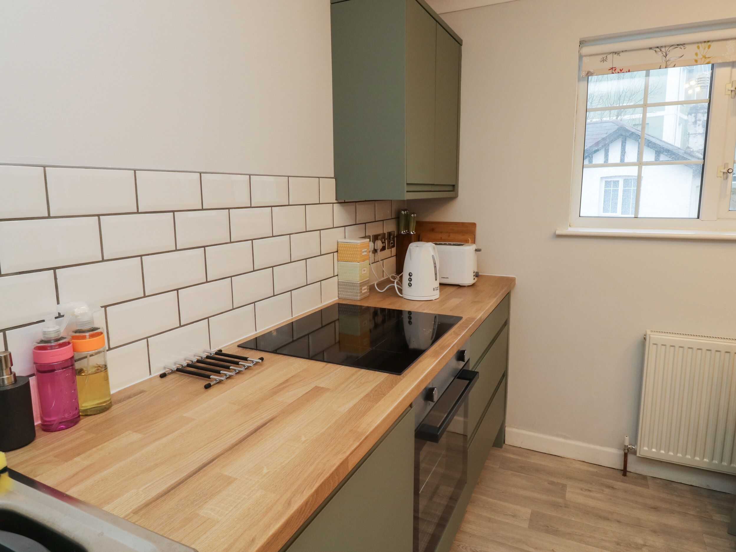 A kitchen with a wooden countertop, a built-in oven, and a window with a view of a house.