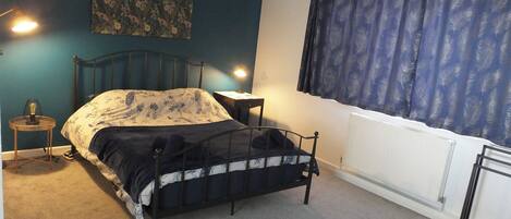 Een slaapkamer met een bed, nachtkastjes, een radiator en een raam met gordijnen.