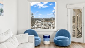 A room with a large window offering a marina view, two blue chairs, a white sofa, and a small blue and white round table. - Moorings 510 - Yacht View Serenity! Top Floor! (Isle of Palms)