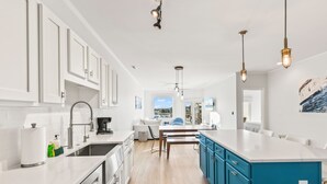 A modern kitchen with white cabinets, a blue island, and a dining area with a view. - Moorings 510 - Yacht View Serenity! Top Floor! (Isle of Palms)