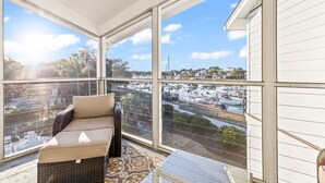 A balcony with wicker furniture, large windows, and a view of a marina and buildings. - Moorings 510 - Yacht View Serenity! Top Floor! (Isle of Palms)