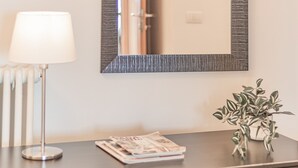 Un escritorio con lámpara, espejo, planta y algunas revistas.