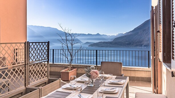 Una terraza con una mesa lista para comer, con vistas a un cuerpo de agua y montañas.