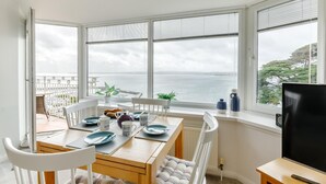 A dining area with a view of the sea, a TV, and a window with blinds. - 2 Bed in Torquay (oc-w28110) (Torquay)