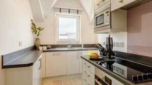 A modern kitchen with a black countertop, white cabinets, a microwave, a stove, and a window with a view. - 2 Bed in Torquay (oc-w28110) (Torquay)