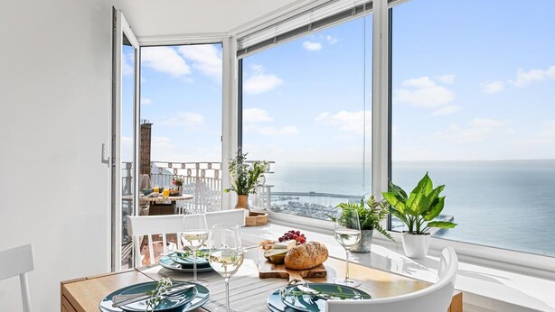 A dining table with plates, glasses, and food, overlooking a coastal view. - 2 Bed in Torquay (oc-w28110) (Torquay)