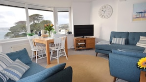 A living room with a sofa, a TV, a dining table with chairs, and a view of the outdoors. - 2 Bed in Torquay (oc-w28110) (Torquay)