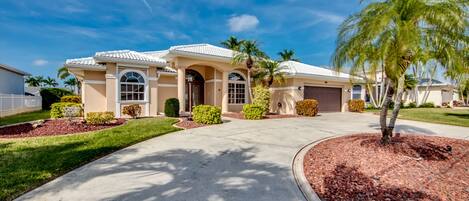 A two-story house with a driveway, palm trees, and a well-maintained lawn.