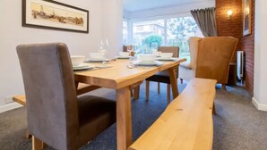 A dining area with a wooden table, four chairs, and a bench. There is a framed picture on the wall, a window with curtains, and a brick wall. - Tynemouth Your Home Away From Home - Pass the Keys (North Shields)