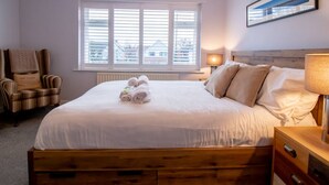 A neatly made bed with rolled towels, a wooden headboard, a chair with a cushion, a bedside lamp, and a window with blinds. - Tynemouth Your Home Away From Home - Pass the Keys (North Shields)