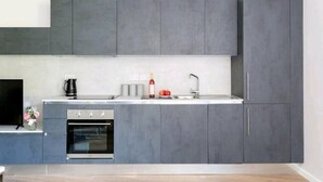 A modern kitchen with grey cabinets, a built-in oven, a sink, and a coffee maker. - Deluxe Central London North Apartment (Greater London)
