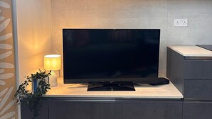 A modern living room with a flat-screen TV on a wooden cabinet, a small table with a lamp, and a potted plant. - Deluxe Central London North Apartment (Greater London)