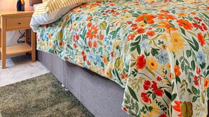 A bedroom with a floral bedspread, a striped pillow, and a nightstand with a lamp. - Deluxe Central London North Apartment (Greater London)