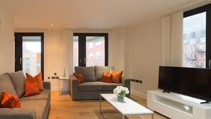 A modern living room with a grey sofa, a white coffee table, and a flat-screen TV on a white entertainment unit. - Capacity House · Central Tower Bridge Apartment (London)