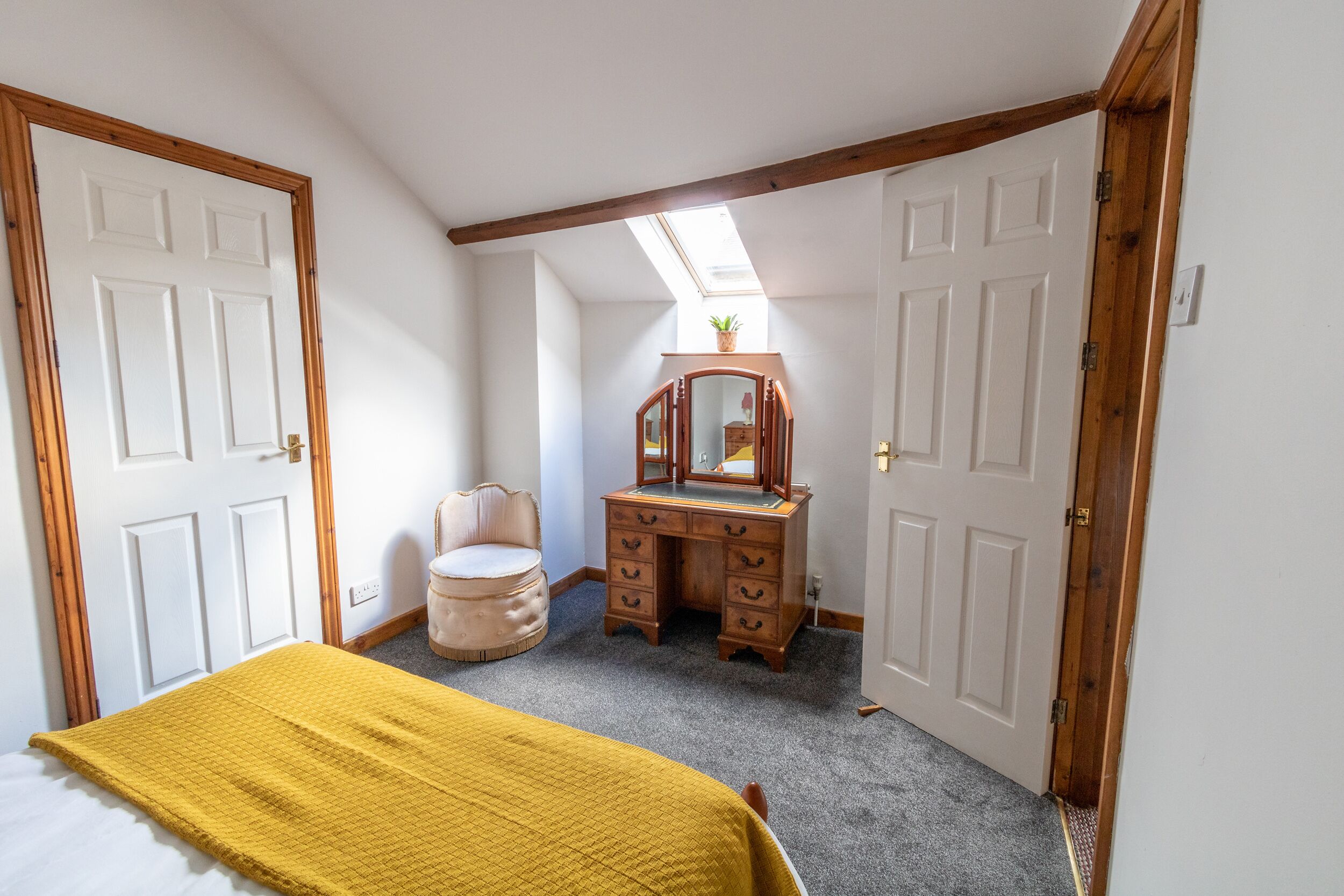 A bedroom with a bed, a dresser, a chair, and a skylight.