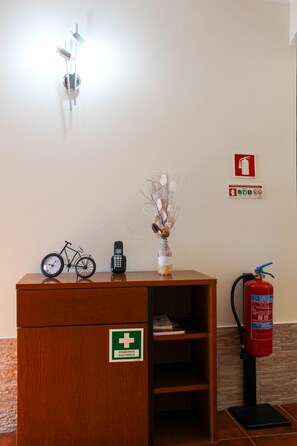 A reception desk with a clock, a vase with dried flowers, a fire extinguisher, and a first aid sign. - Vieira Rooms Natural Pools (Ponta Delgada)