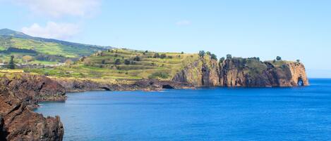 A coastal landscape with a prominent rocky cliff and a clear blue sea.