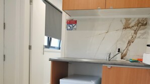 A compact kitchen with a built-in refrigerator, a sink, and wooden cabinets. - Quarto com Kitchenet junto ao Metro (Senhora da Hora)