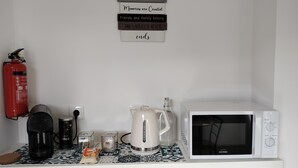 A kitchen counter with a coffee maker, kettle, and microwave. A fire extinguisher is mounted on the wall. - Quarto com Kitchenet junto ao Metro (Senhora da Hora)