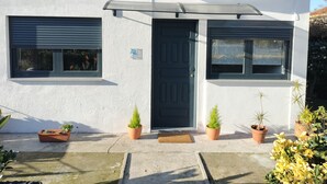 A modern building with a black door, two windows with shutters, and a small awning over the entrance. - Quarto com Kitchenet junto ao Metro (Senhora da Hora)