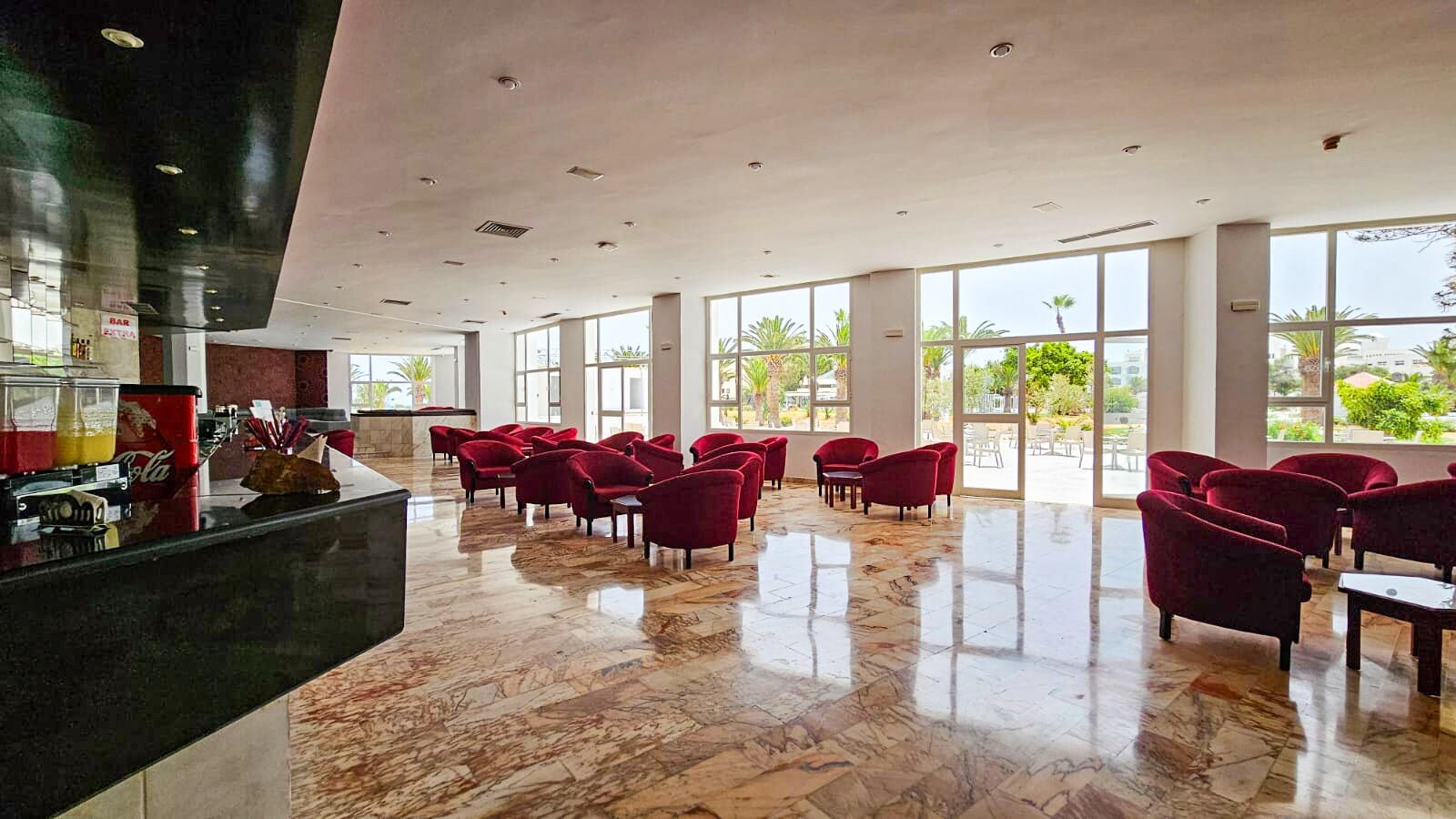 Un hall d’entrée spacieux, doté d’un sol en marbre, de rangées de fauteuils rouges et de grandes fenêtres offrant une vue sur l’extérieur.