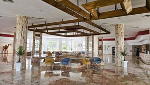A spacious lobby with marble flooring, wooden beams, and a seating area with yellow and blue chairs. - Monarque El Fatimi Mahdia (Mahdia)