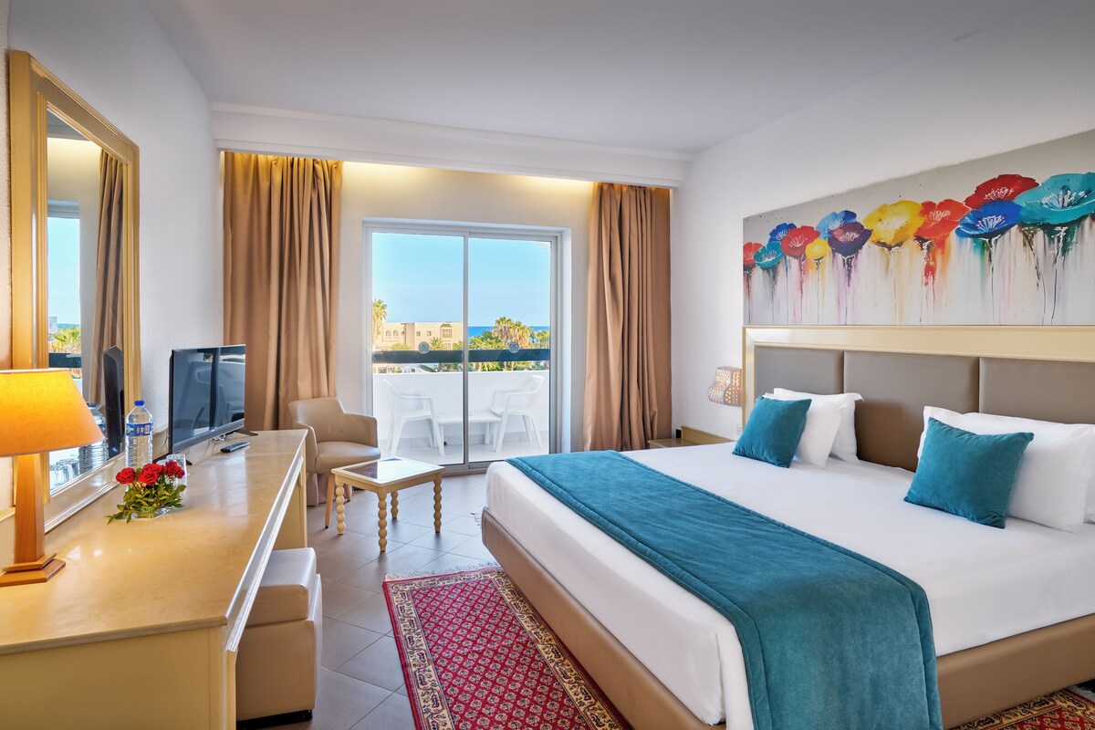 A hotel room with a bed, a desk with a computer, a chair, a TV, and a view of the outdoors.