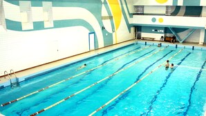 An indoor swimming pool with multiple lanes, a diving board, and a lifeguard chair.