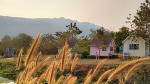 Un paisaje rural con casas, una masa de agua y montañas al fondo.