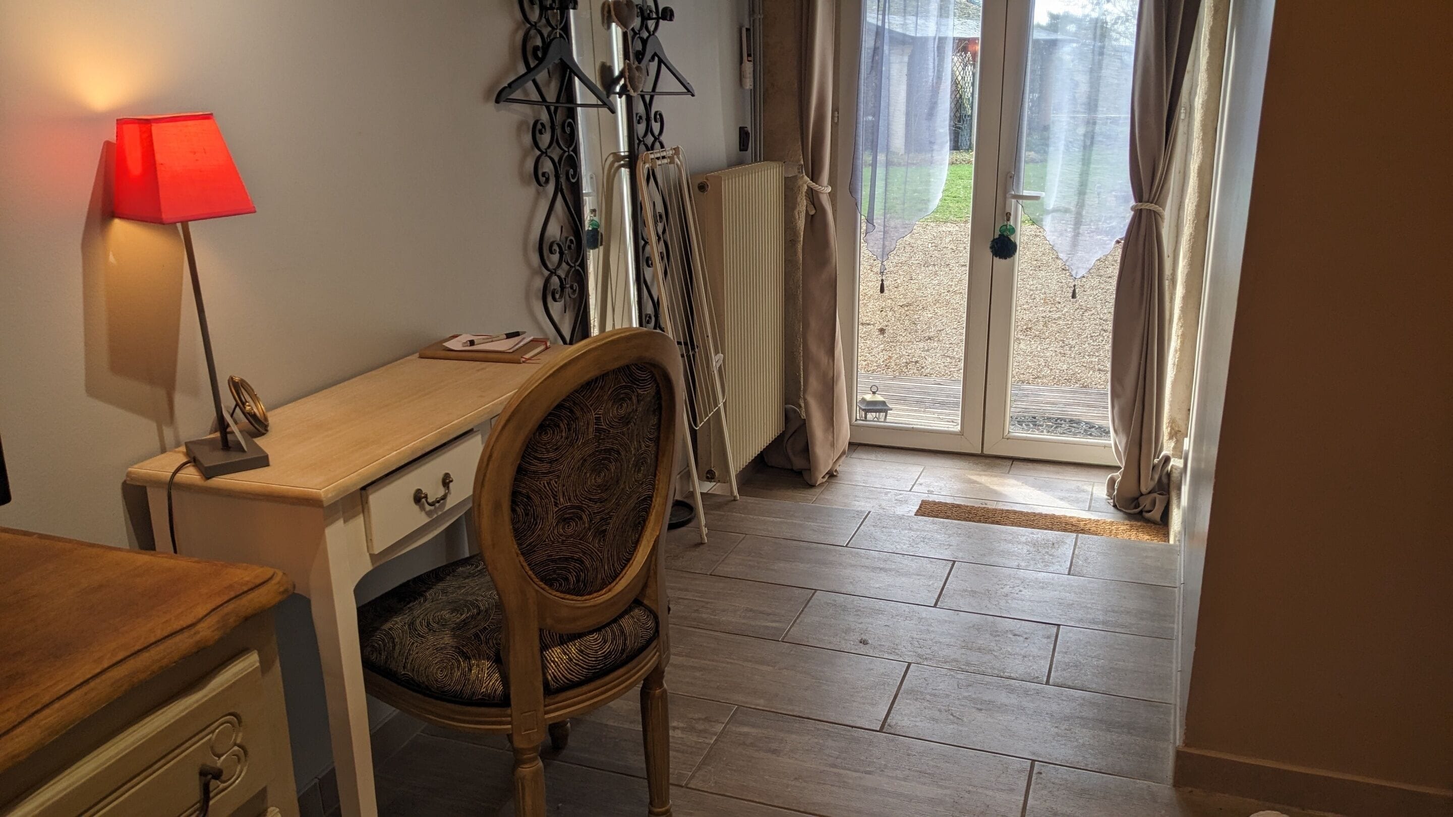 Une pièce avec un bureau en bois, une chaise dotée d’un coussin à motifs, une lampe rouge et un radiateur.