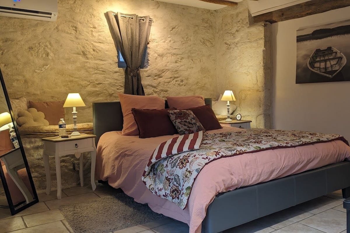 Een slaapkamer met een bed, twee nachtkastjes met lampen, een spiegel, een stenen muur en een schilderij.