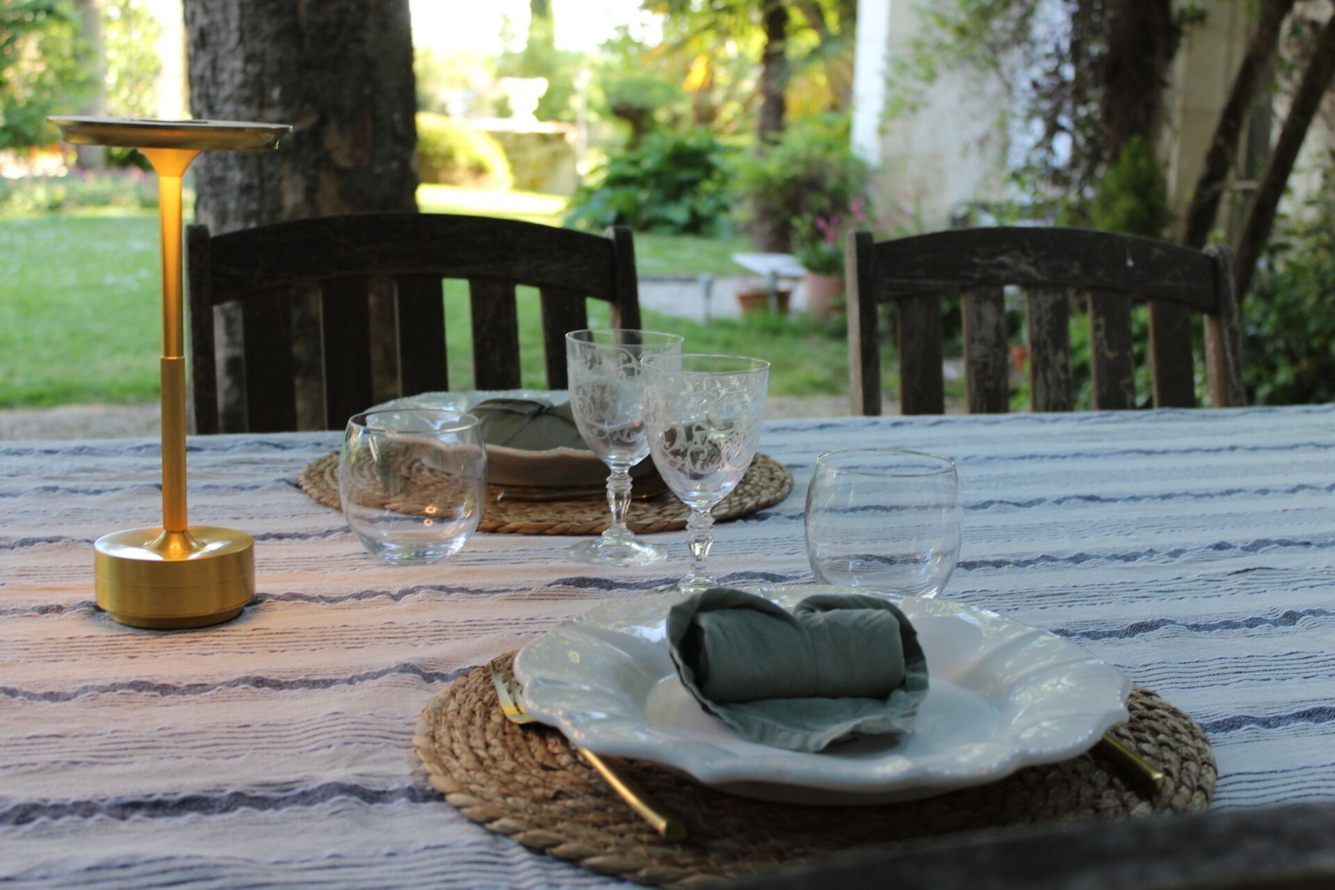 A table set outdoors with a placemat, a plate with a cushion, and three glasses.