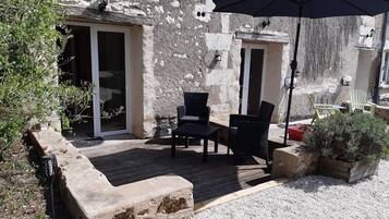 An outdoor patio with a wooden deck, black wicker furniture, and a blue umbrella.