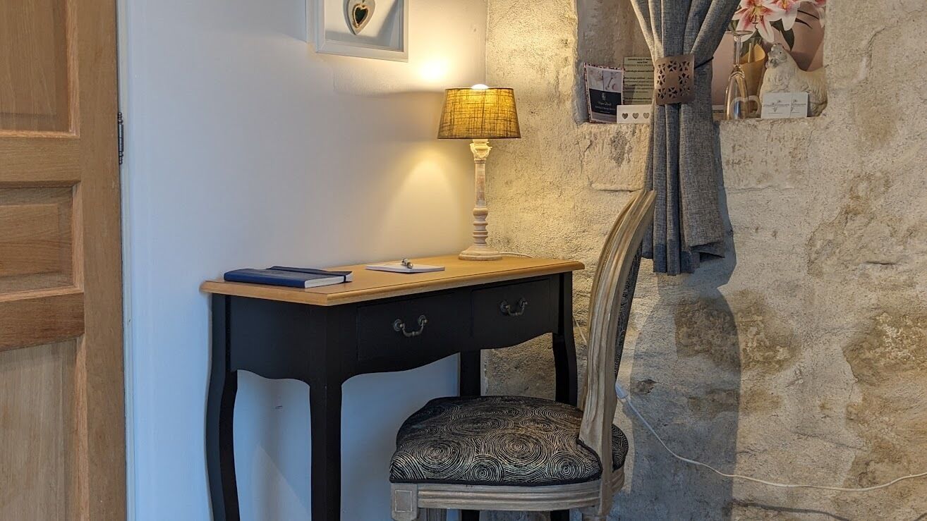 Un espacio de trabajo con escritorio, silla, lámpara y una estantería adosada a la pared decorada con objetos.