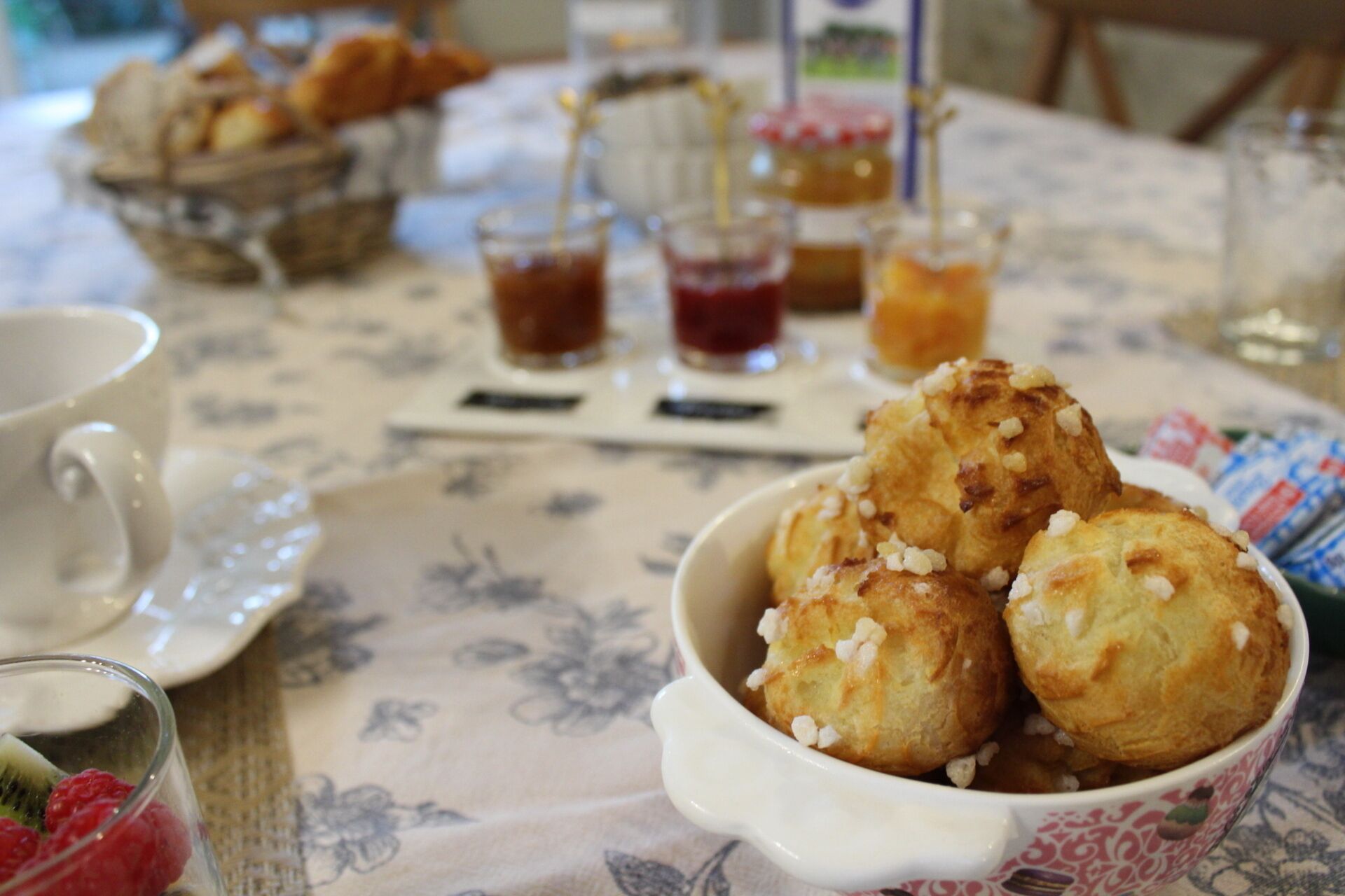 A table with a floral tablecloth, a bowl of pastries, and a cup of tea.