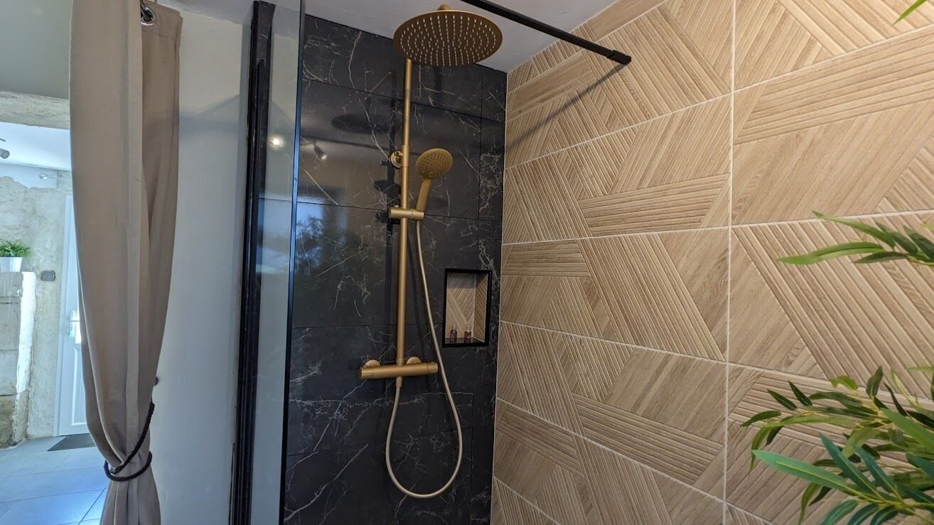 Une douche moderne avec un pommeau de douche doré et un pommeau de douche à main, le tout installé sur un mur de marbre orné de carreaux aux motifs géométriques.
