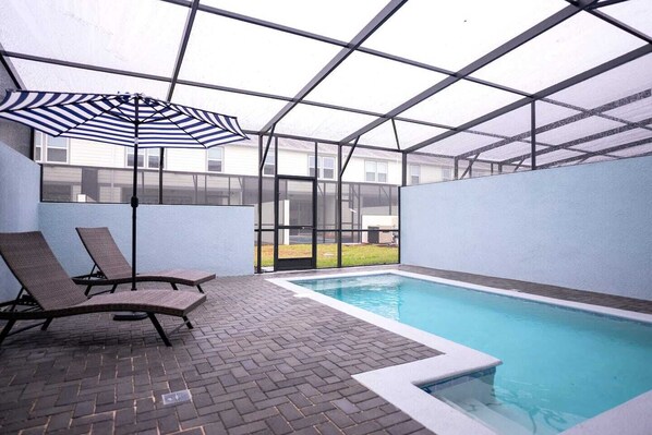 An indoor swimming pool with lounge chairs and a striped umbrella.