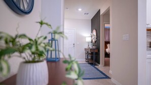Ein Flur mit Blumentopf, blauem Teppich, einer Tür und einem Spiegel an der Wand.
