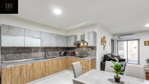 Een moderne keuken met grijze kastjes, een houten aanrecht en een eethoek met een tafel en stoelen.