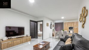 Een moderne woonkamer met een grote flatscreen-televisie, een houten salontafel en een zwarte leren bank.