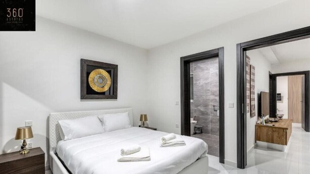 Een moderne hotelkamer met een groot bed, een nachtkastje met lamp, een lijst met kunstwerk aan de muur en een houten bankje in de hoek.