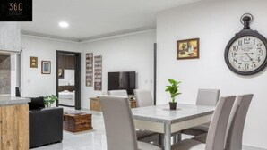 Een moderne woonkamer met een eethoek, een grote wandklok en een televisie.