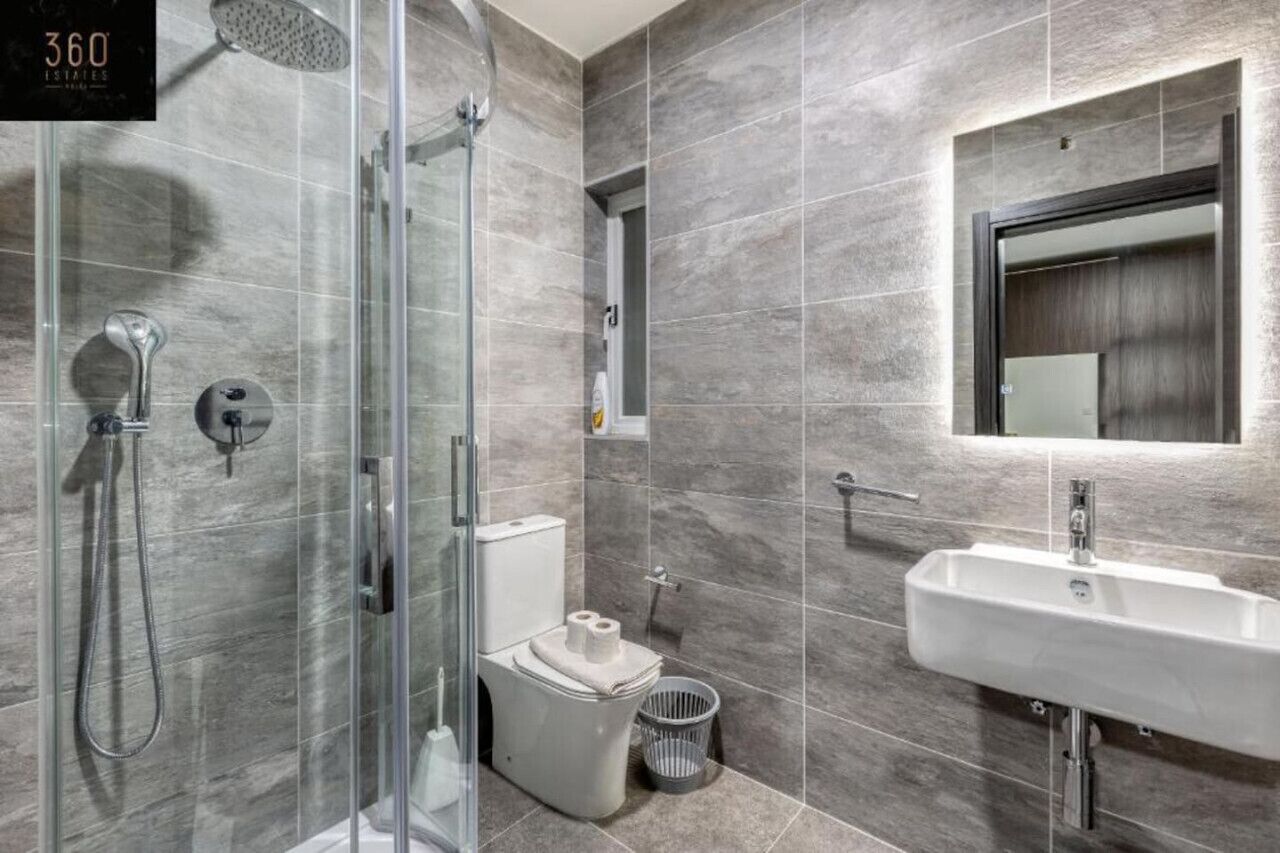 Une salle de bain moderne dotée d’une douche à parois de verre, de toilettes, d’un lavabo et d’un grand miroir.