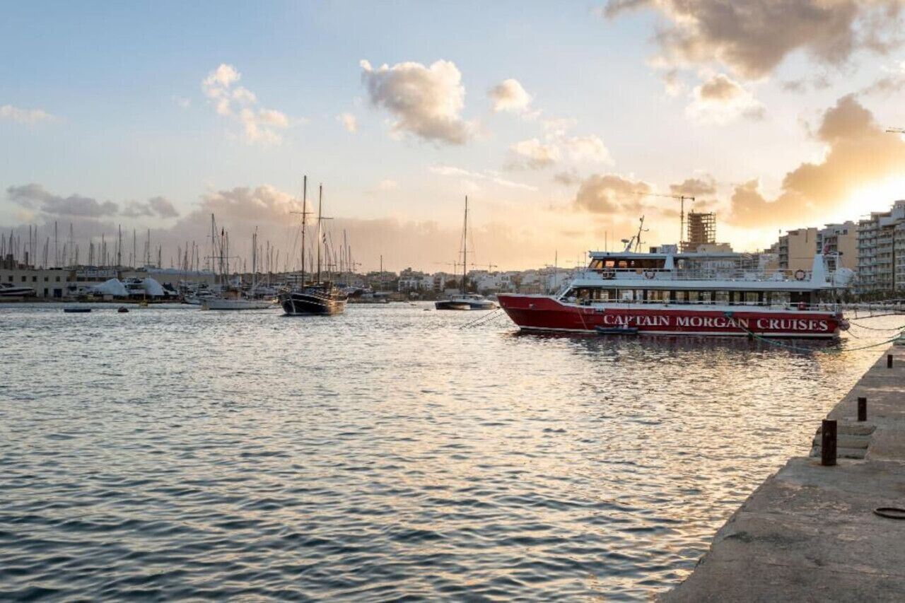 Een jachthaven met aangemeerde boten, waaronder een opvallende rode en witte cruiseschip dat 'Captain Morgan Cruises' heet.